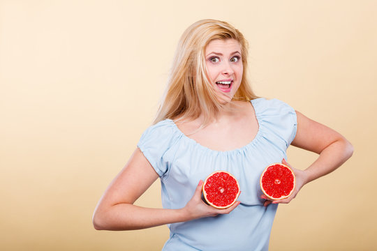 Woman holding red grapefruit on breast