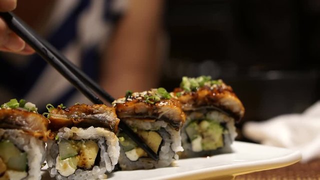 Hand using chopsticks picking eel avocado with cheese sushi roll