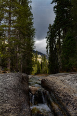 Amazing perspective of a stream meandering down some rocks in Sequoia and Kings Canyon National Park on a stormy day with sun light illuminated the mountains in the background.