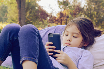 little girl laying on daddy's tummy and watching on smart phone with blurry green park background, filtered tones