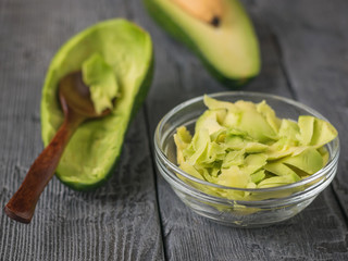 The flesh of the avocado in a glass bowl on a wooden table with a spoon. Vegetarian food.