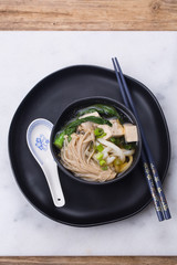 Japanese udon noodle soup with enoki mushroom, tofu and Gai lan. Black ceramic bowl and a plate 