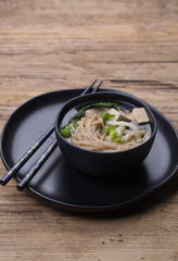 Japanese udon noodle soup with enoki mushroom, tofu and Gai lan. Black ceramic bowl and a plate 