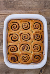 Twelve cinnamon buns in baking dish, not frosted. Rustic wood tabletop. 