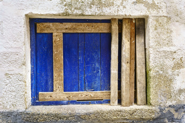 Walled window with a blue board and unpainted horizontal and vertical timbers in the frame of a very old stone house