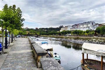 View of the Betanzos river from one of the banks with small boats moored and an iron bridge in the background