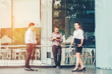 Businessman using a digital tablet office outdoors and Blurred People Walking in Front of Modern Office Building