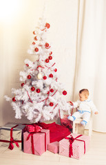 Baby 1 year old sitting on gift box with Christmas tree. Merry Christmas. Holiday season.