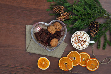 Coffee with marshmallow, bumps, nuts, chocolate and branches of a Christmas tree on a wooden table. View from above. Christmas and New Year. Still life.