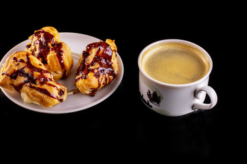 Cake eclair with chocolate icing, cup of coffee, chocolate, on a black background