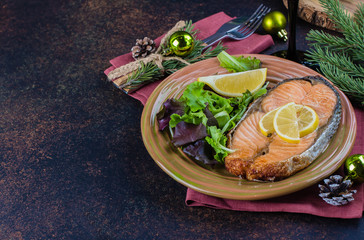 Christmas Dinner Table Setting. Delicious salmon steak grilled on plate with lemon and assorted salad on dark stone table background. Top view, copy space
