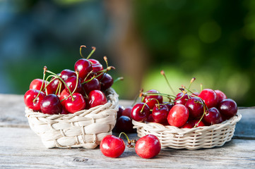 Basket with a cherry on a wooden table on a background of a green garden.