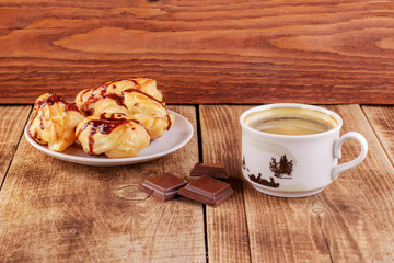 Cake eclair with chocolate icing on a white dish, cup of coffee, chocolate