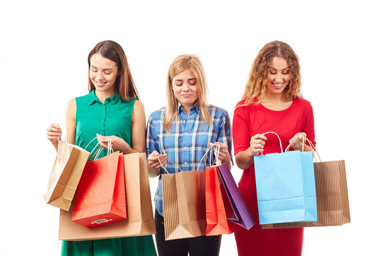 Portrait of three young girlfriends holding bunches of multi-colored shopping bags