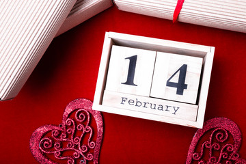 Wooden calendar show of February 14 with red heart and gift boxes.