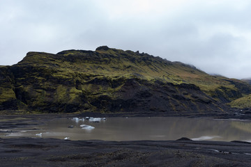 Green and black hills and little glacial lake