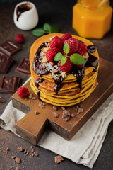 Pumpkin pancakes with fresh raspberries, chocolate and walnuts on dark stone or concrete background. Selective focus.