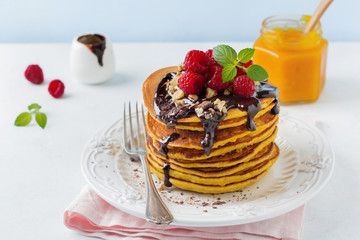 Pumpkin pancakes with fresh raspberries, chocolate and walnuts on  light stone or concrete background. Selective focus.