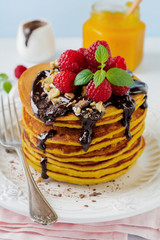 Pumpkin pancakes with fresh raspberries, chocolate and walnuts on  light stone or concrete background. Selective focus.