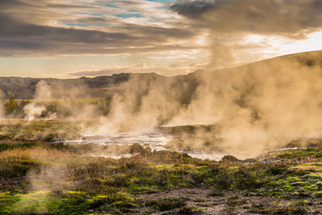 Nebelschwaden über dem großen Geysir in Island bei Sonnenuntergang, 