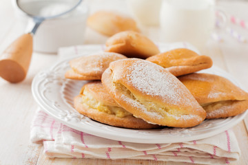 Pasties with cottage cheese and powdered sugar on a light wooden background. Traditional Russian pastry Sochnik. Selective focus. .