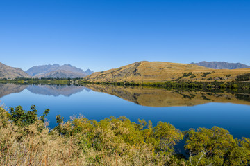 Fototapeta na wymiar Reflections on Lake Hayes on a sunny day with clear sky, Queenstown, New Zealand.