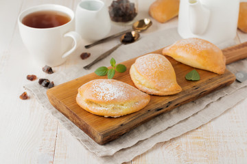 Pasties with cottage cheese and powdered sugar on a light wooden background. Traditional Russian pastry Sochnik. Selective focus. .