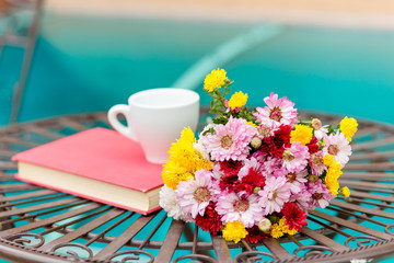 Bright colorful chrysanthemum flowers with coffee cup and book on the forged table
