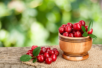 Cranberry with leaf in wooden bowl on old wooden table with blurry garden background