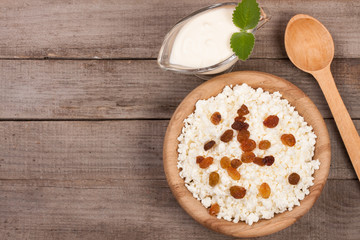 Cottage cheese in bowl with sour cream and raisins on old wooden background with copy space for your text. Top view
