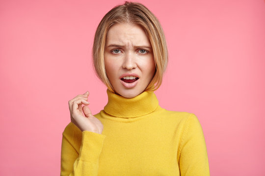 Upset discontent light haired female opens mouth in dissatisfaction, being displeased with bad news or comments, has unhappy expression, isolated over pink background. Disappointment and displeasure