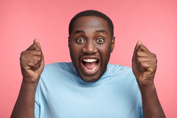 Successful African American male achieves cherished goal, looks excited and amazed, clenches fists,...