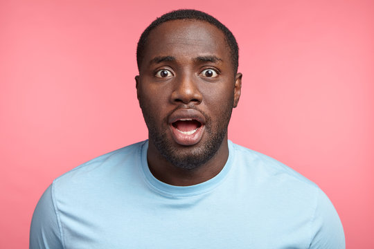 Stunned amazed dark skinned male model shocked to have successful business deal, isolated over pink background. Surprised black student wonders because of unexpected final exam at end of month