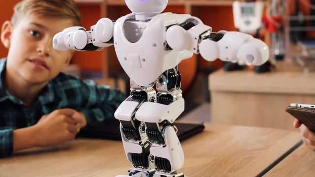 Close up of little white robot operated by a tablet device moving in front of the kids on the table in the playing room. Portrait shot
