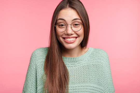Portrait of smiling female student looks happily through spectacles, glad to have stroll on street and coffee shop meeting. Asian woman rests after work at home, has charming smile, poses in studio