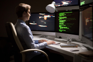 Profile view of confident middle-aged programmer in eyeglasses sitting in front of modern computer...