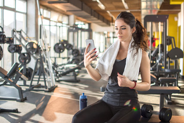 Sporty girl with towel around shoulders using phone in gym.
