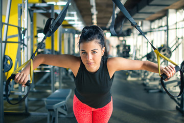 Fototapeta na wymiar Young attractive woman having suspension training with fitness straps in the gym.