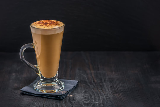 coffee latte in glass with froth of milk on black paper napkin over wooden table
