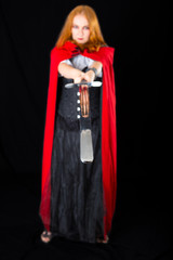 Fototapeta na wymiar woman wearing in black long gown and red cloak brandishing twohanded sword (focus on swords end)