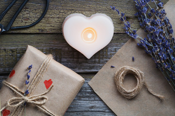 Top view of the gift in a kraft paper, the bouquet with lavender and the candle in shape of heart on the old wooden background. Copy space.