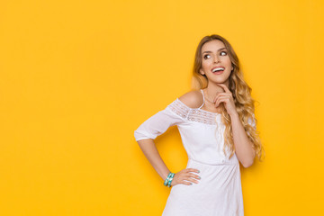 Fototapeta na wymiar Smiling Beautiful Blond Young Woman In White Summer Dress Is Looking Away And Thinking