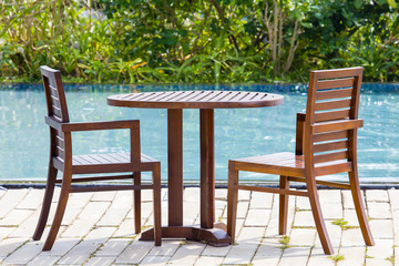 Wooden table and two chairs in empty cafe next to the swimming pool, Thailand