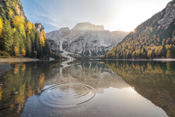 The sunset at the Braies Lake inthe autumn season with beautiful colored trees, water circle, reflections and the sun light, Dolomites, Trentino-Alto Adige, Italy