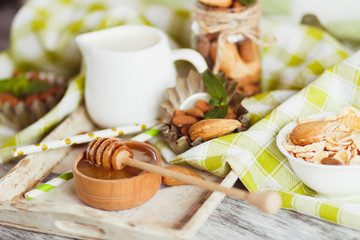 Honey in the bowl, muesli, mint leaves, almonds and jar with milk on the wooden tray