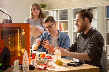 Group of young engineers carrying out quality inspection of prototype made with help of 3D printer...