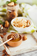 Honey in the bowl, muesli, mint leaves, almonds and jar with milk on the wooden tray