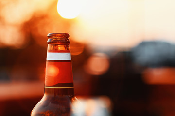 Beer Bottle Against Summer Sky At Sunset On Blurry Background With Lens Flare