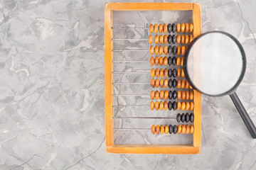 Old wooden abacus beside magnifier with black plastic handle on cracked gray concrete