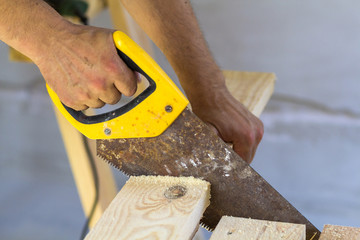 Carpenter hand with saw cutting wooden boards